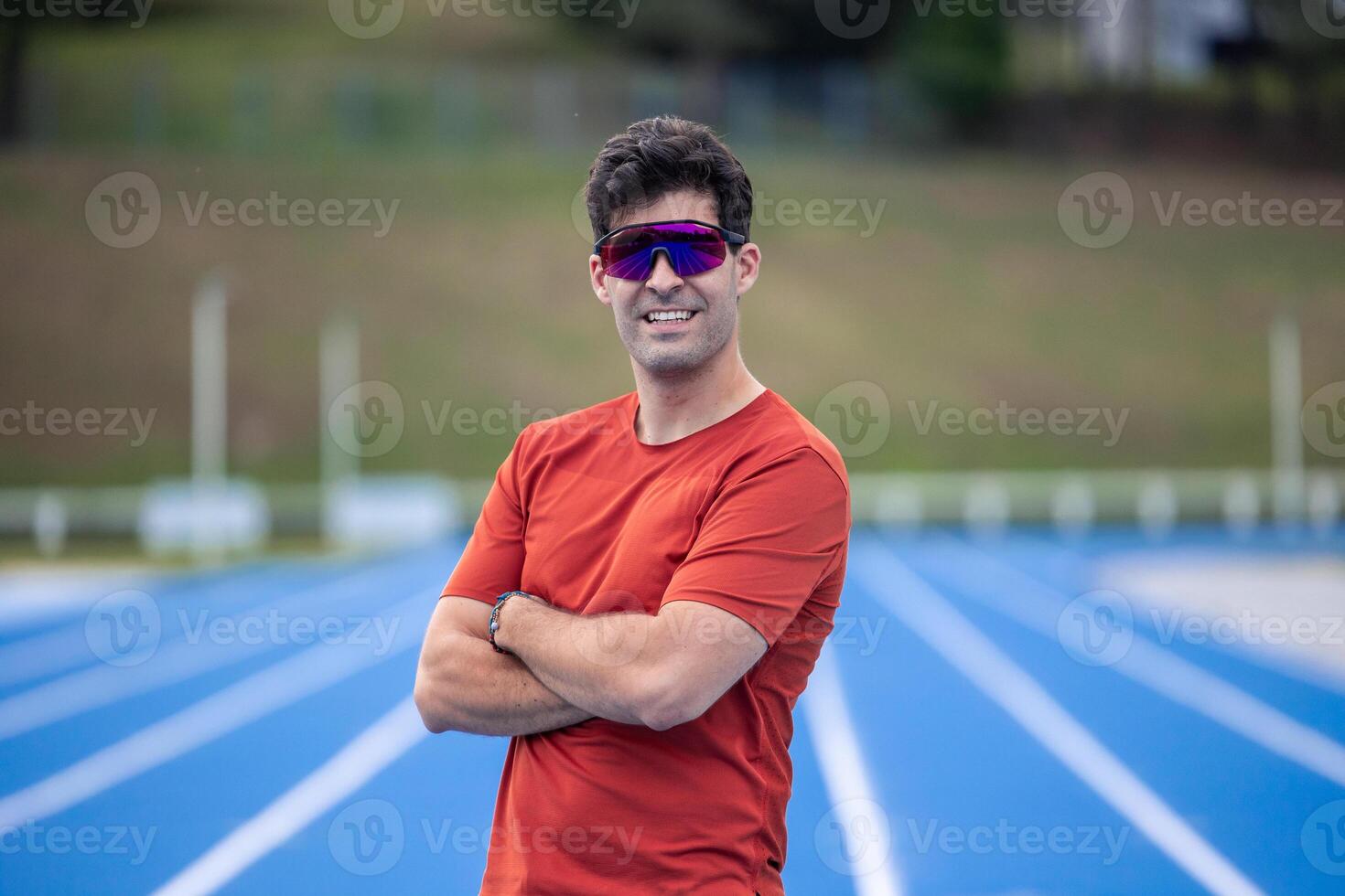 Runner with Sunglasses Smiling at Camera on Blue Athletic Track photo