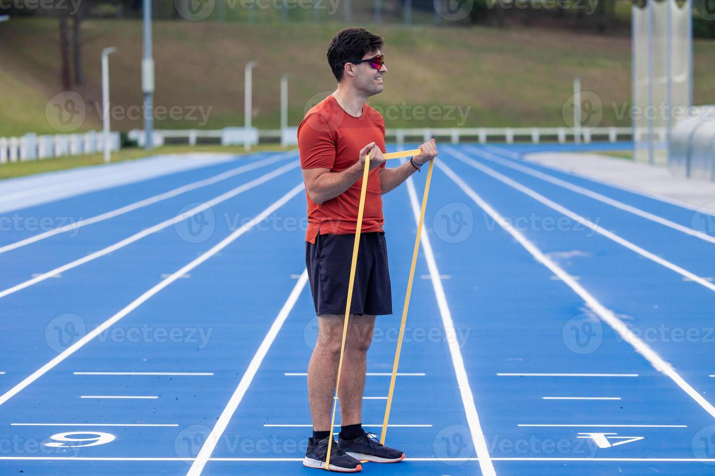 Sportsman with Sunglasses Strengthens Biceps with Resistance Band on Outdoor Athletic Track photo
