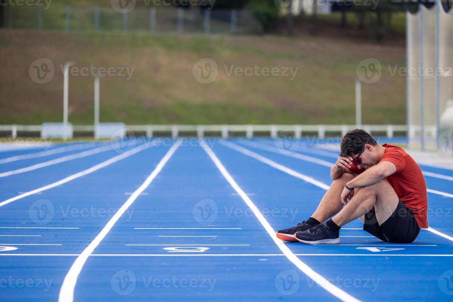 copyspace Exhausted Runner with a Face of Suffering Sits on the Ground at the Finish Line of an Athletic Track photo
