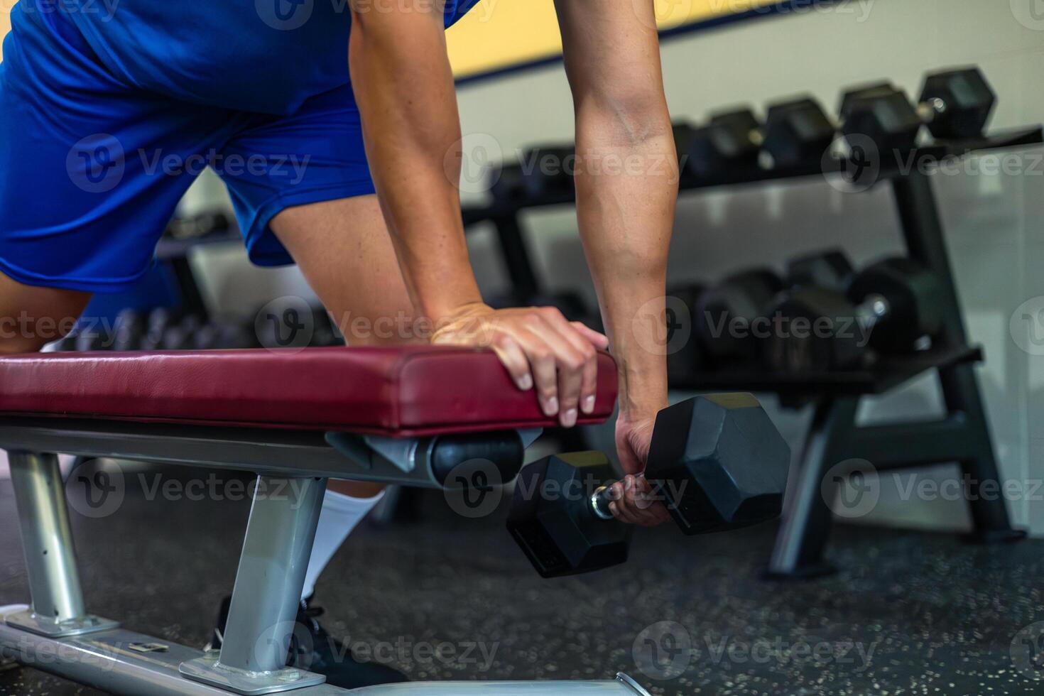 close-up of anonymous athlete holding weight dumbbell while exercising on gym bench photo
