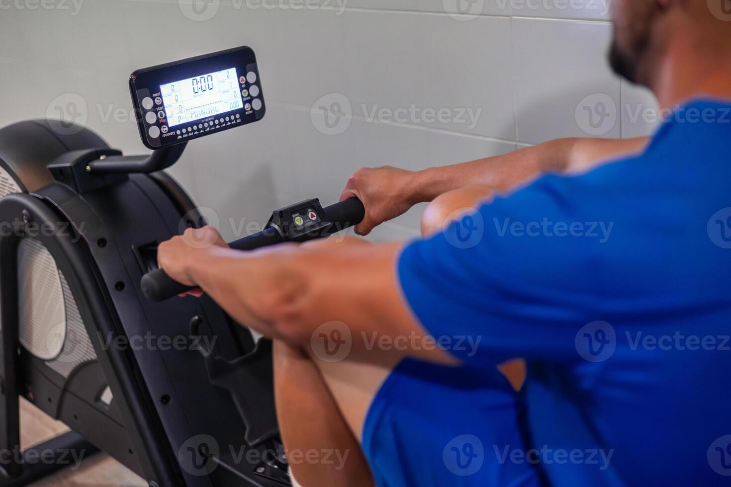closeup of anonymous young athlete performing aerobic exercise on rowing machine in gym photo
