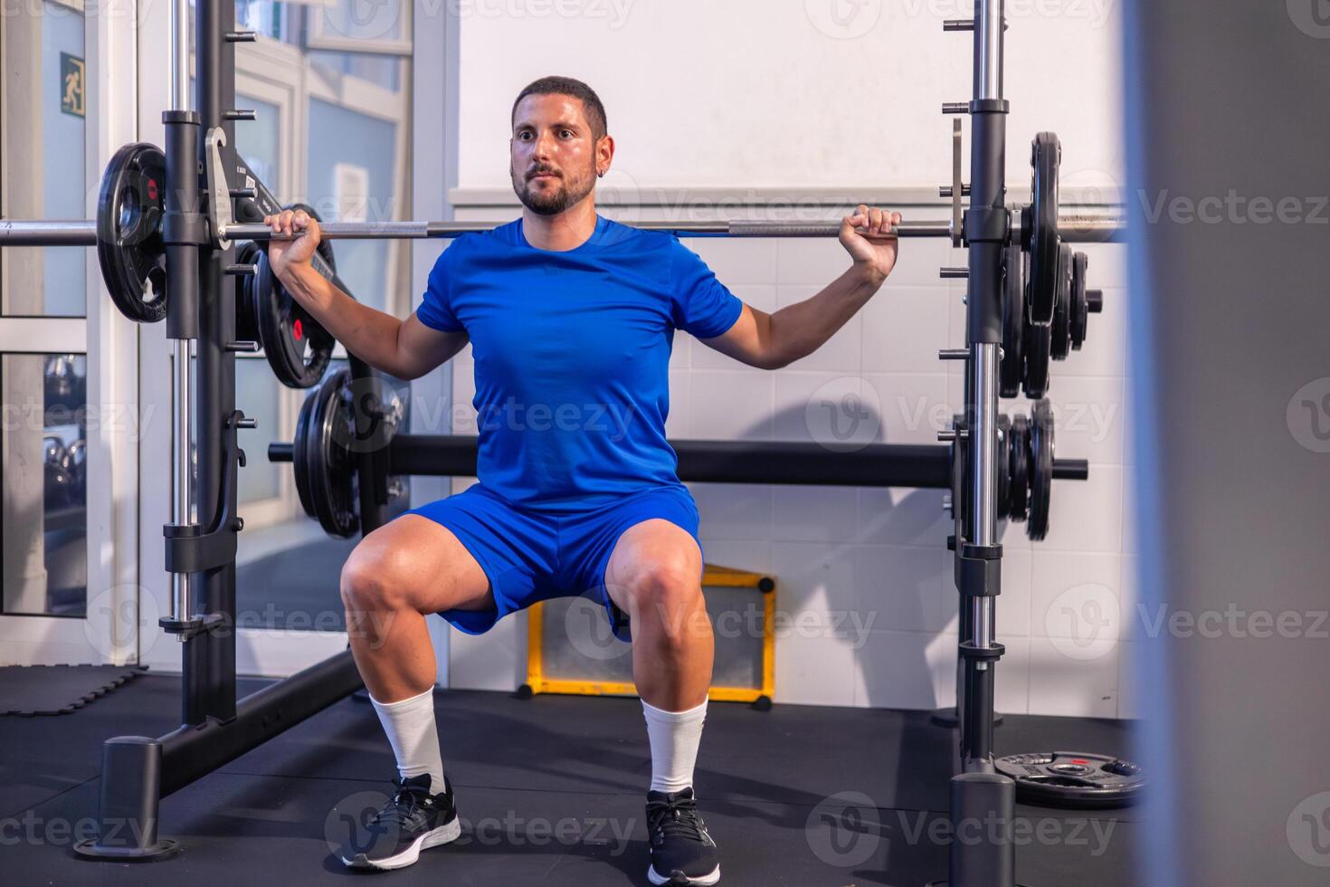 Young Fitness Athlete Performing Squats with Weight on Multi Power Machine at Gym photo