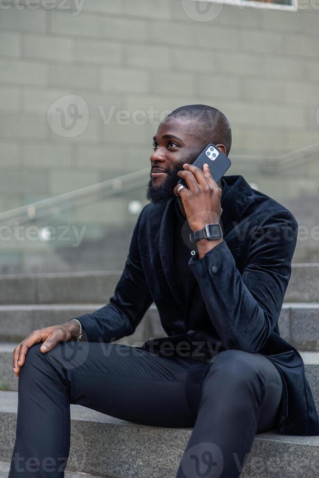 vertical African American businessman in suit talking on mobile phone while seated on downtown steps photo