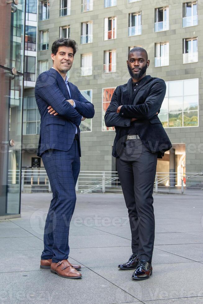 vertical African and Hispanic businessmen in suits posing with crossed arms in financial district photo