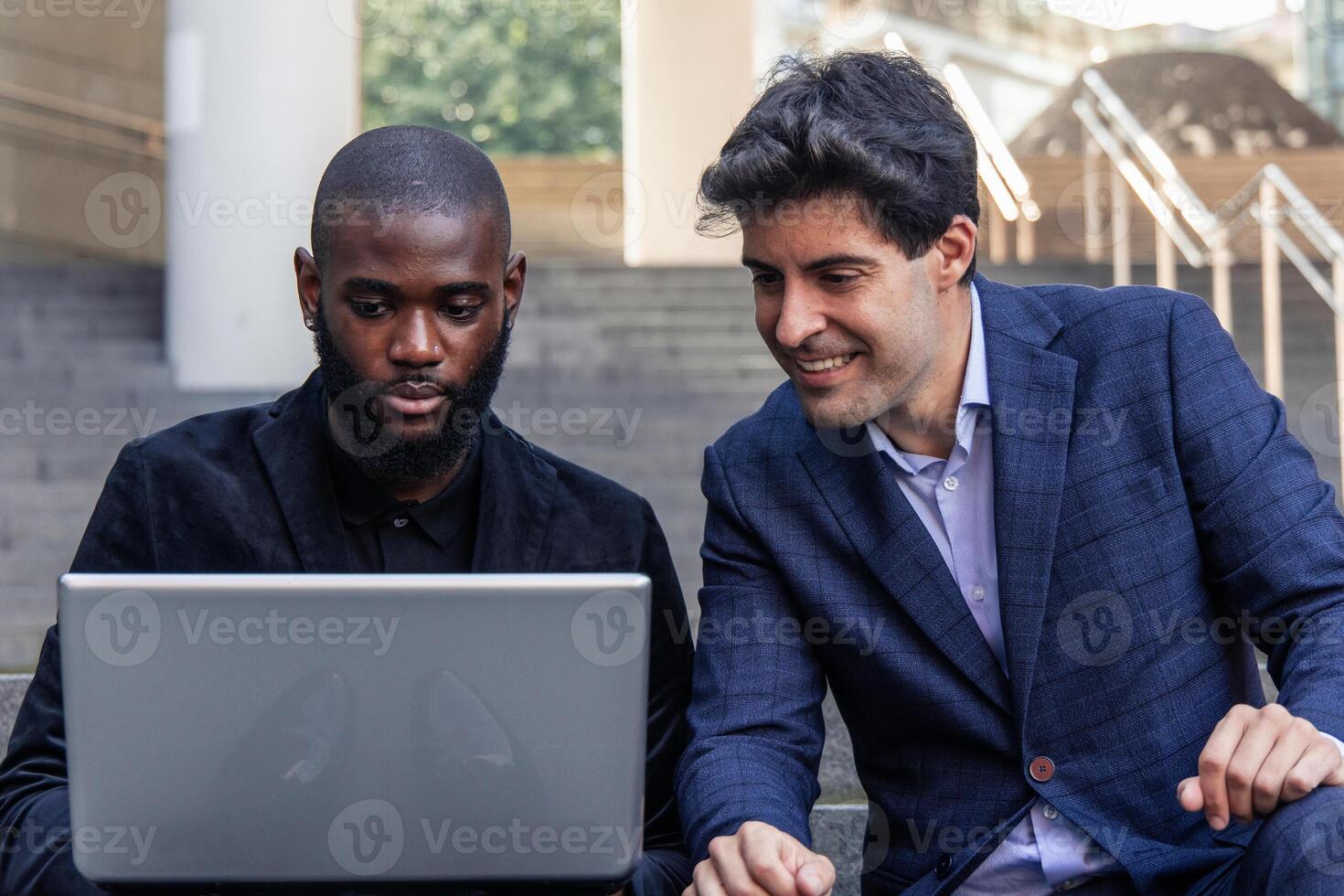closeup African and Hispanic businessmen reviewing project on laptop outdoors in financial district photo