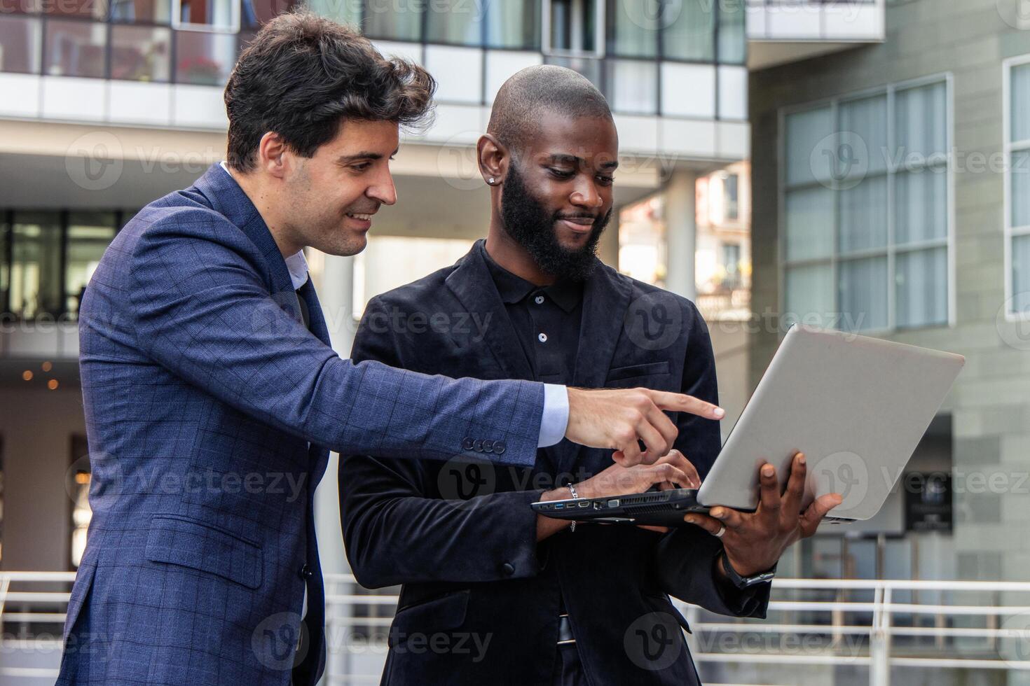 African businessman holds laptop while Hispanic colleague points at screen to emphasize data photo