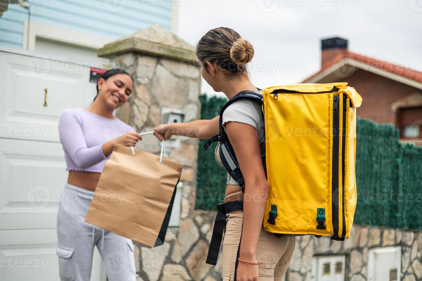 Delivery worker girl, viewed from behind handing food to a Latina customer at her doorstep photo