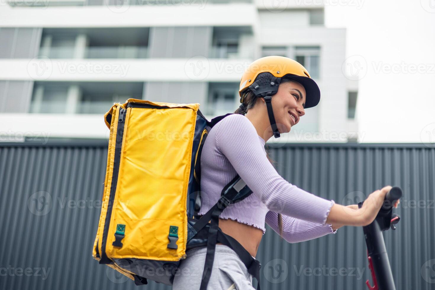 closeup low-angle shot of food delivery girl on electric scooter with yellow backpack in urban area photo