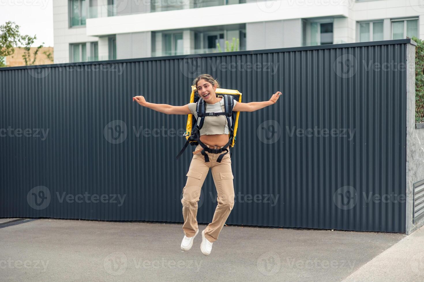 hispanic food delivery girl with braces jumping happily with arms extended against dark background photo