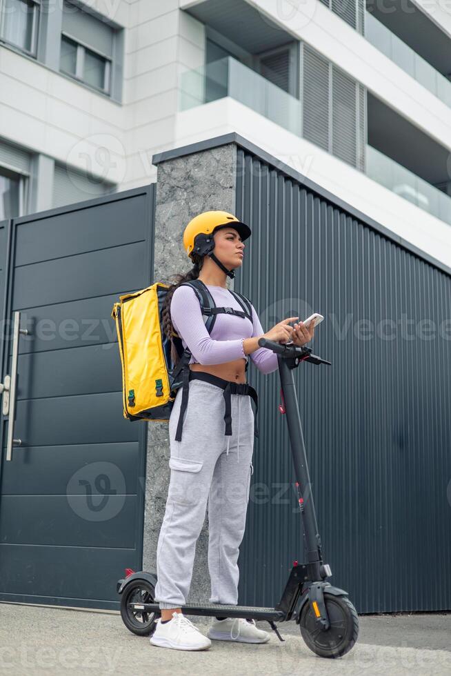 vertical latin food delivery girl with yellow backpack searching for client address on smartphone photo
