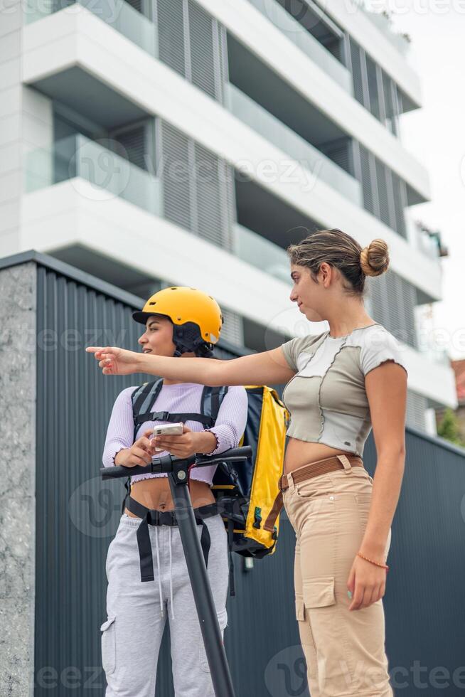 latin food delivery girl with yellow backpack and helmet receiving directions from passerby photo