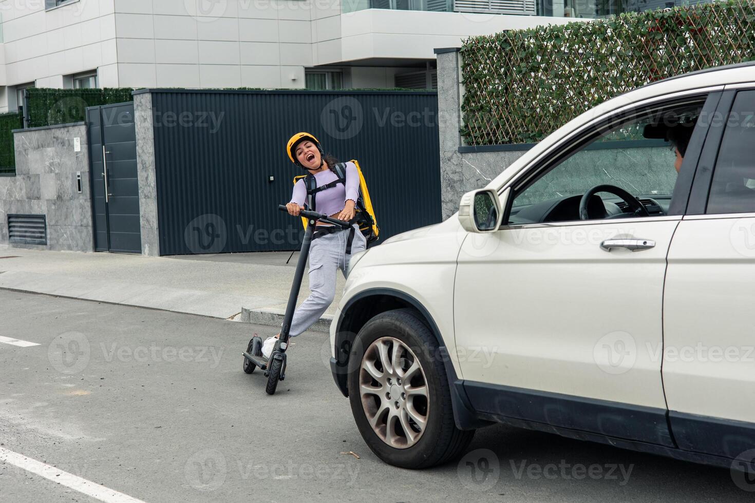 Latin food courier with yellow backpack and electric scooter screaming in fear as car approaches photo