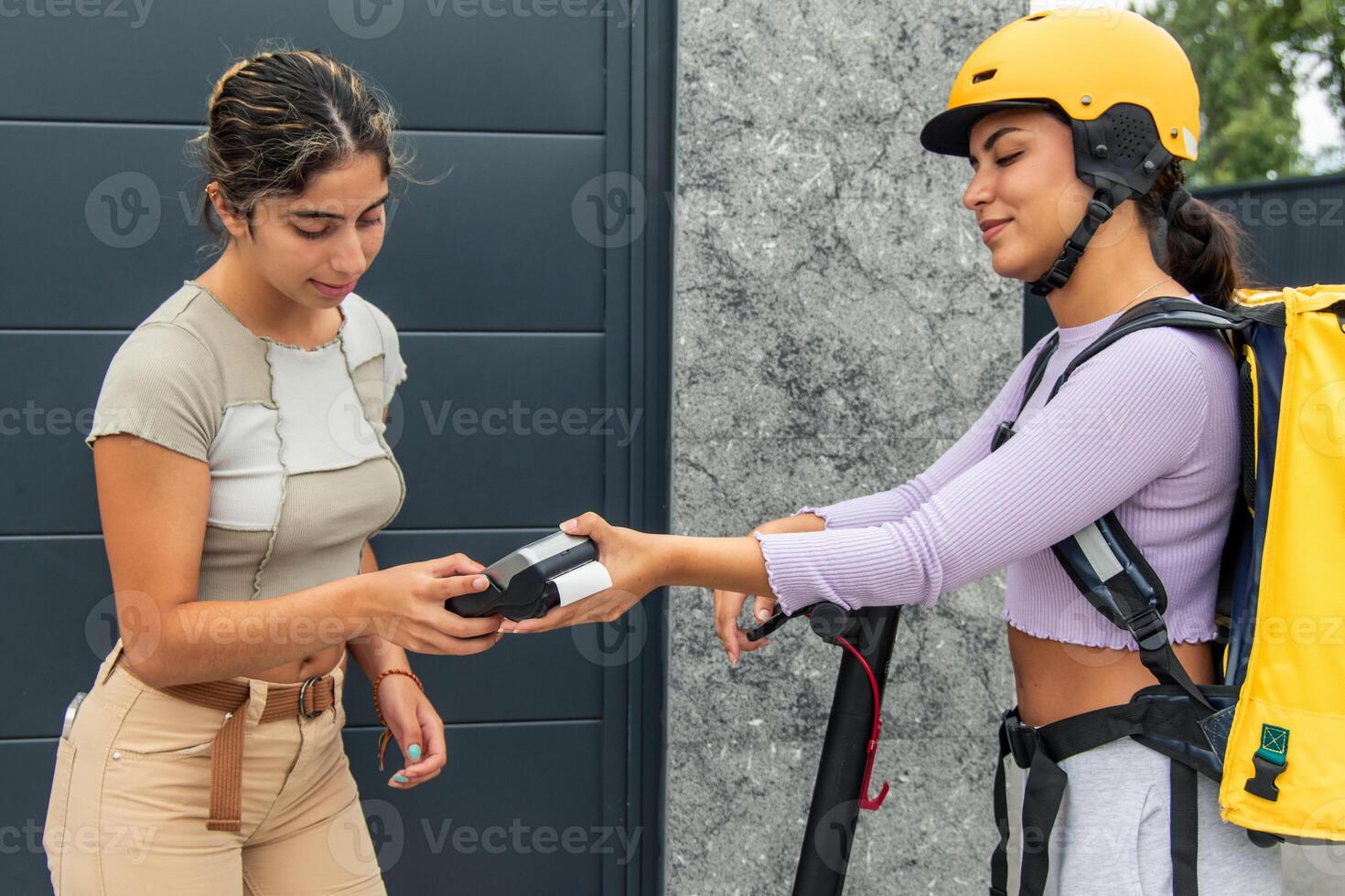 Client entering PIN on payment terminal offered by Latin courier with yellow backpack and helmet photo