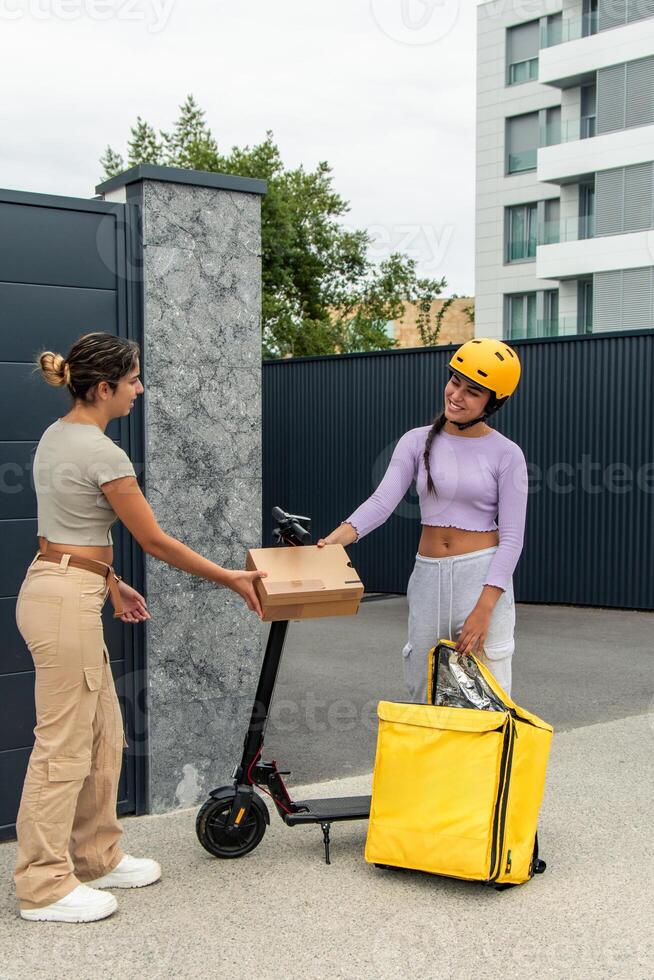 vertical Latin courier with helmet and electric scooter removing package from backpack for delivery photo
