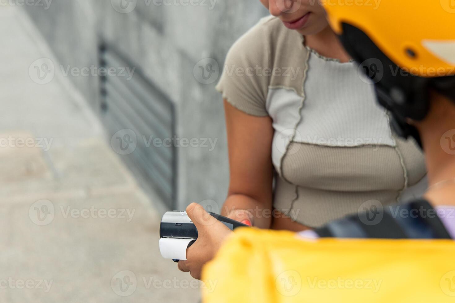 unrecognized courier with yellow backpack and helmet holding payment terminal while client pays photo