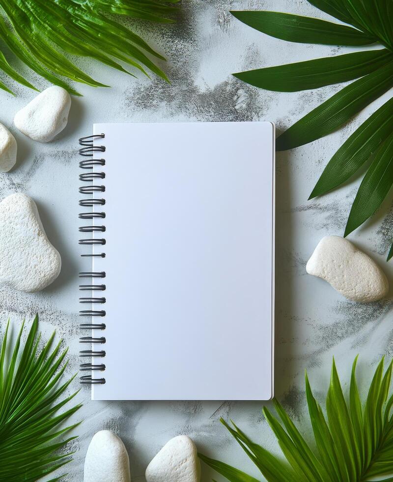 Blank notebook surrounded by greenery and stones on a marble surface for creative inspiration photo