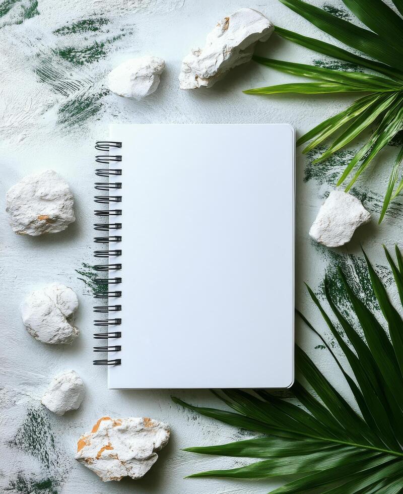 Blank notebook surrounded by greenery and stones on a marble surface for creative inspiration photo