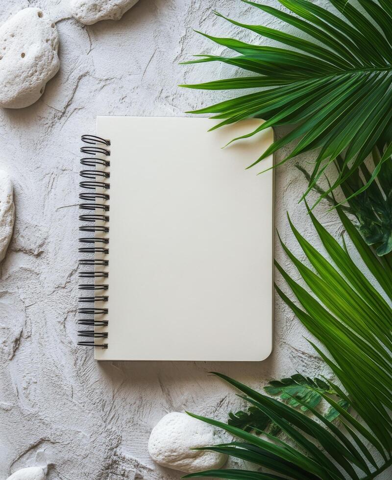 Blank notebook surrounded by greenery and stones on a marble surface for creative inspiration photo