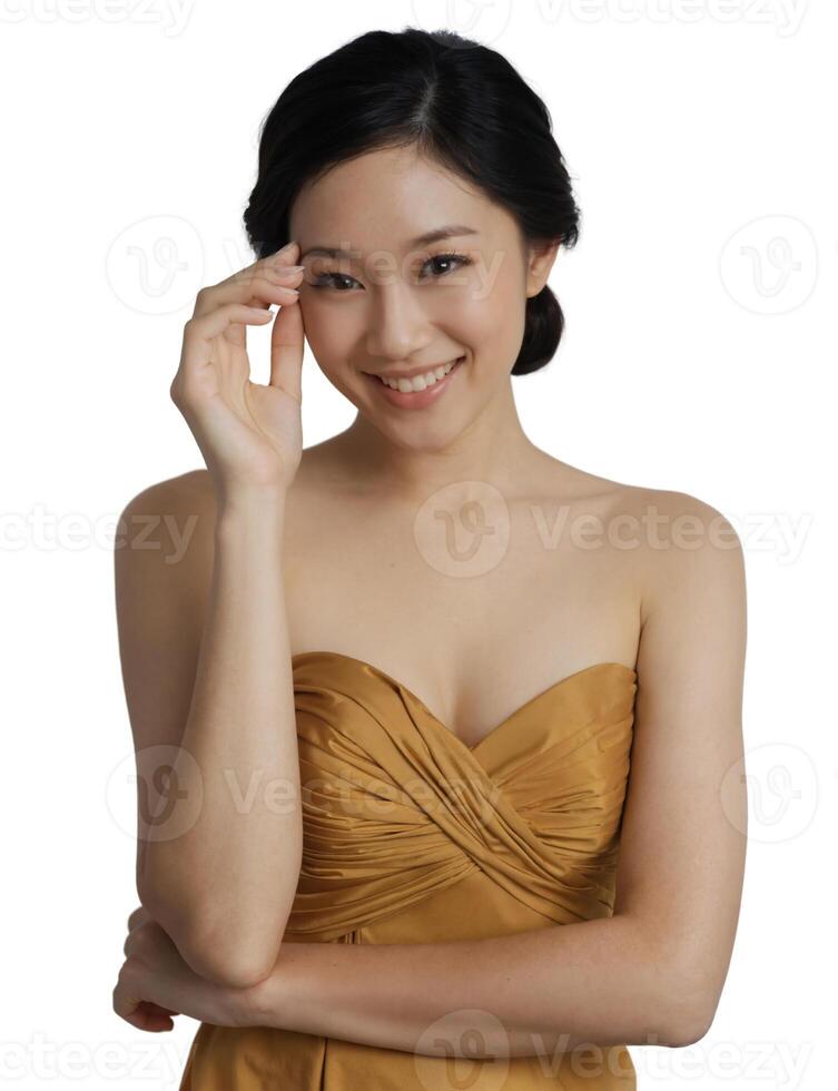 A smiling Asian woman with a bun hairstyle, wearing a strapless brown dress, against a light background. photo