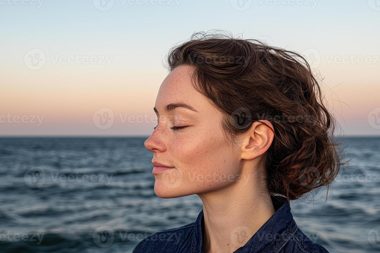 Woman closes her eyes and breathes in the fresh sea air at sunset photo