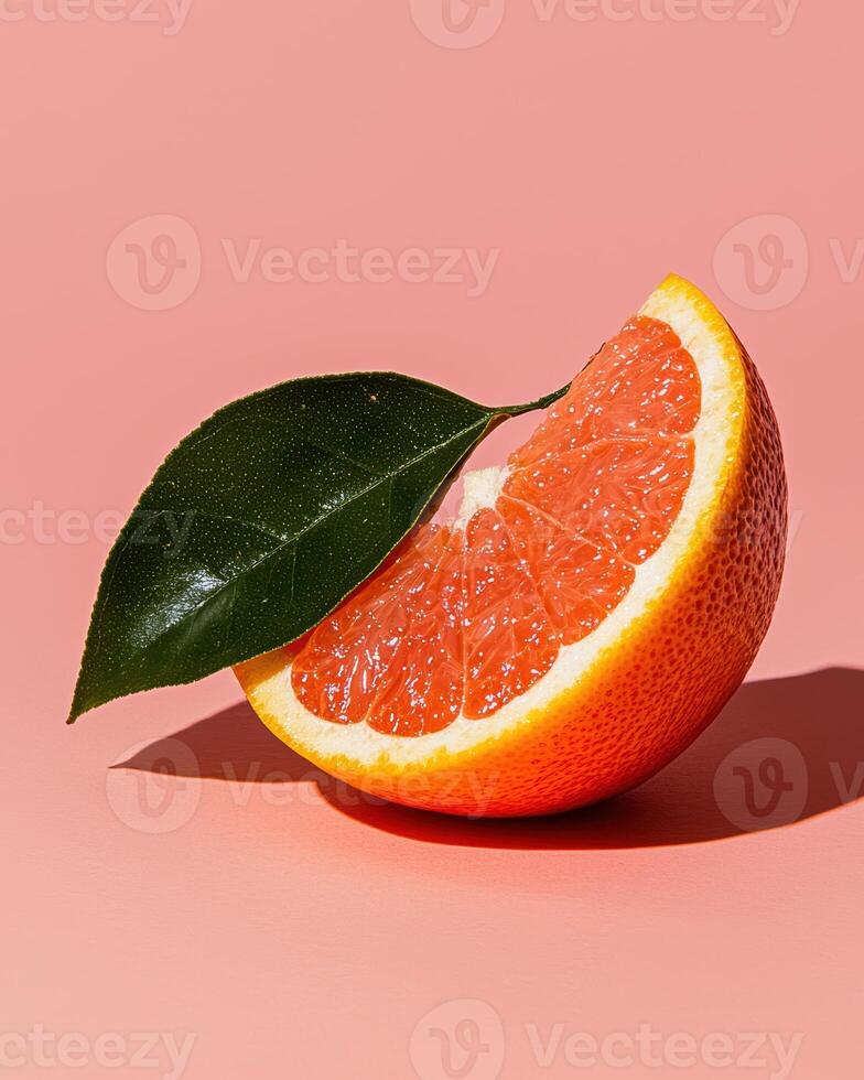 Close up of a juicy grapefruit slice with a green leaf on a pink background photo