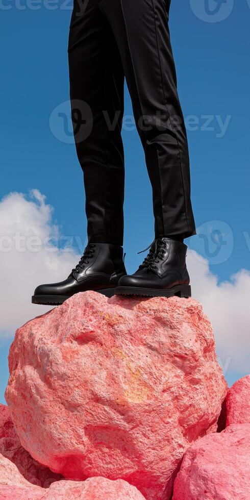 Man in black pants and boots standing on a pink rock against a blue sky photo