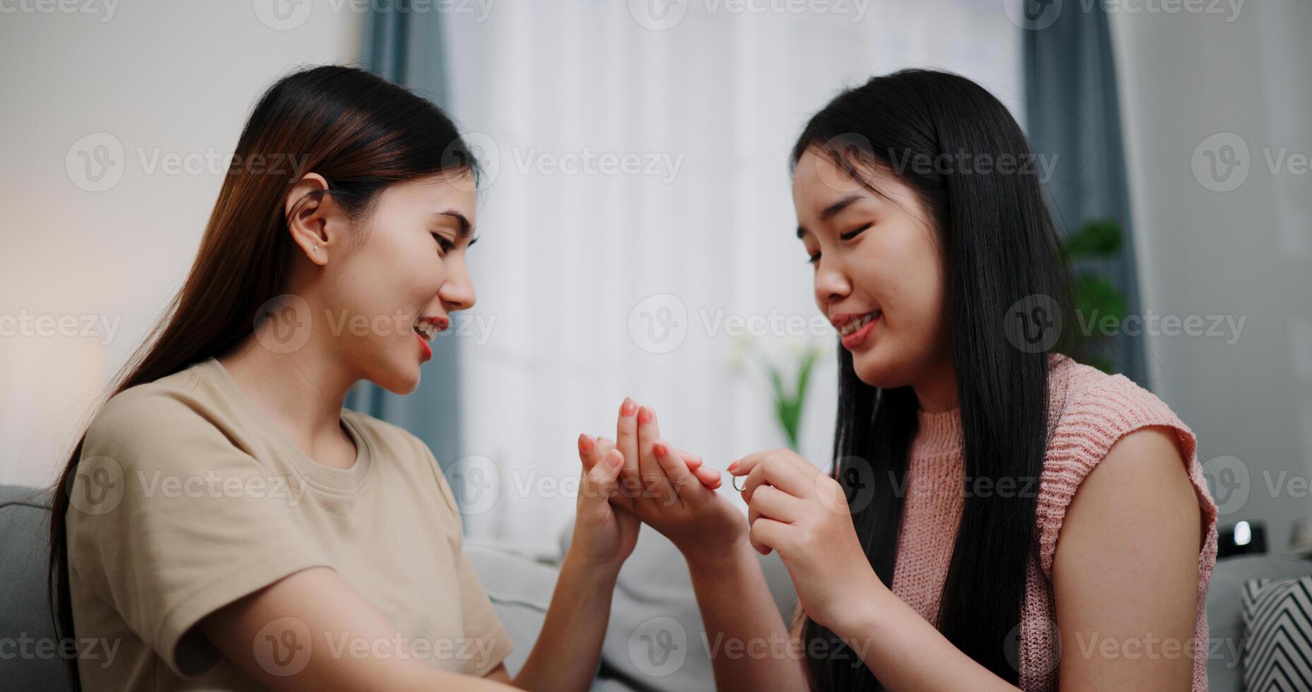 Portrait of Asian lesbian surprises girlfriend with proposal with wedding ring and smiles happily during romantic moment in living room at home. Asian LGBTQ couple. photo