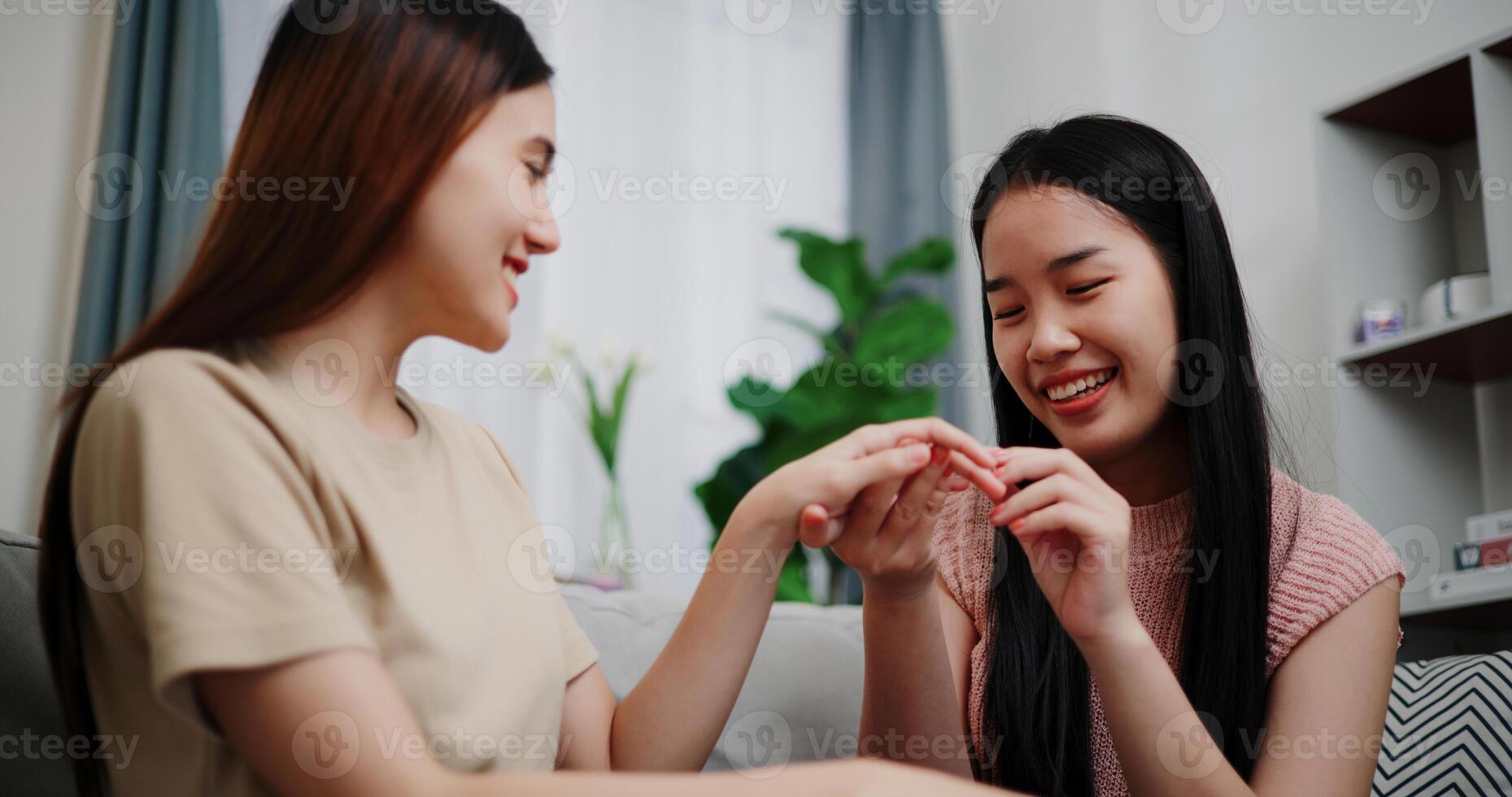 Selective focus, Asian lesbian surprises girlfriend with proposal with wedding ring and smiles happily during romantic moment in living room at home. Asian LGBTQ couple. photo