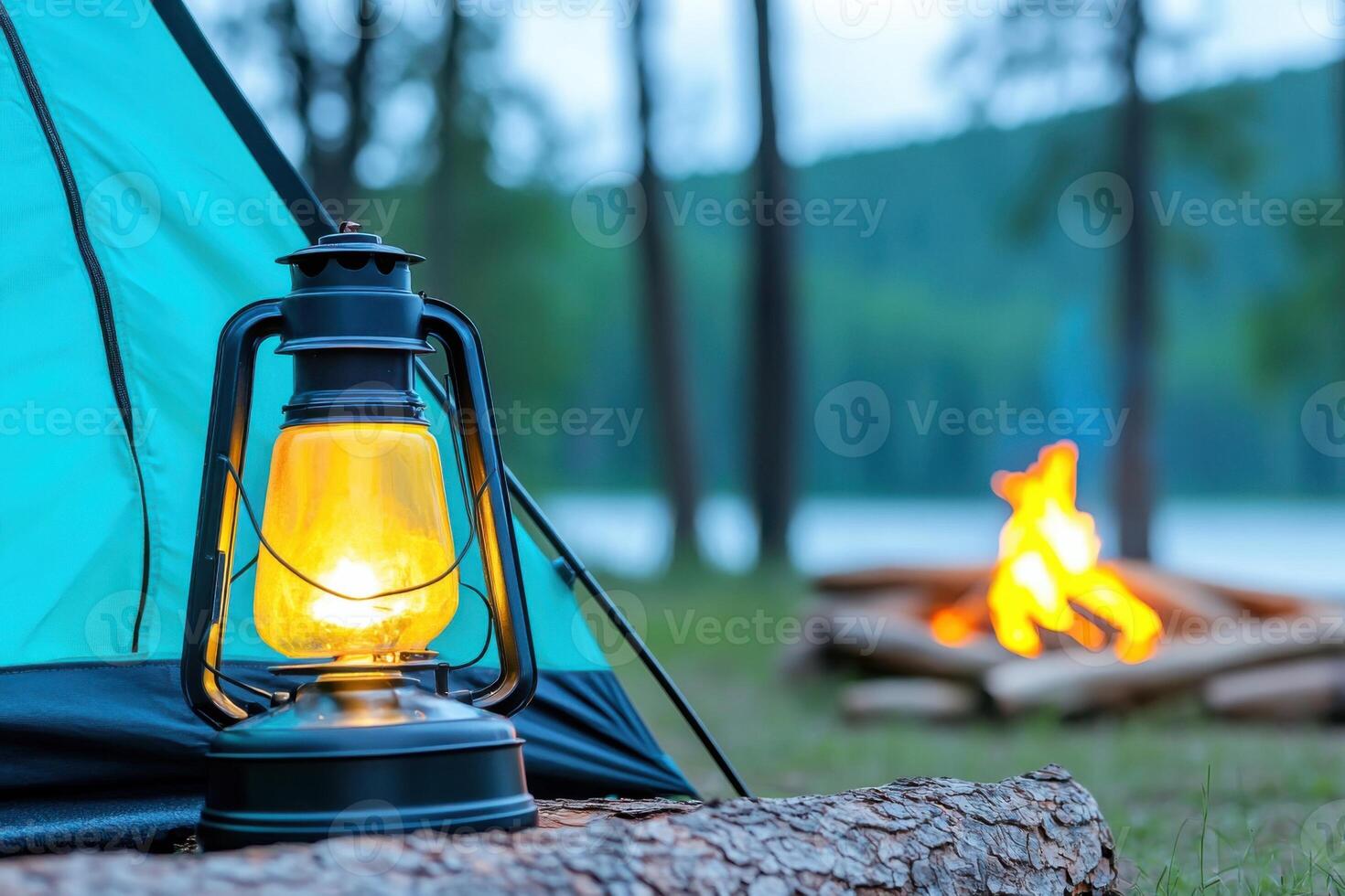 Glowing lantern lights up olive green tent beside terracotta fire pit at dusk in serene camping location near water surrounded by trees photo