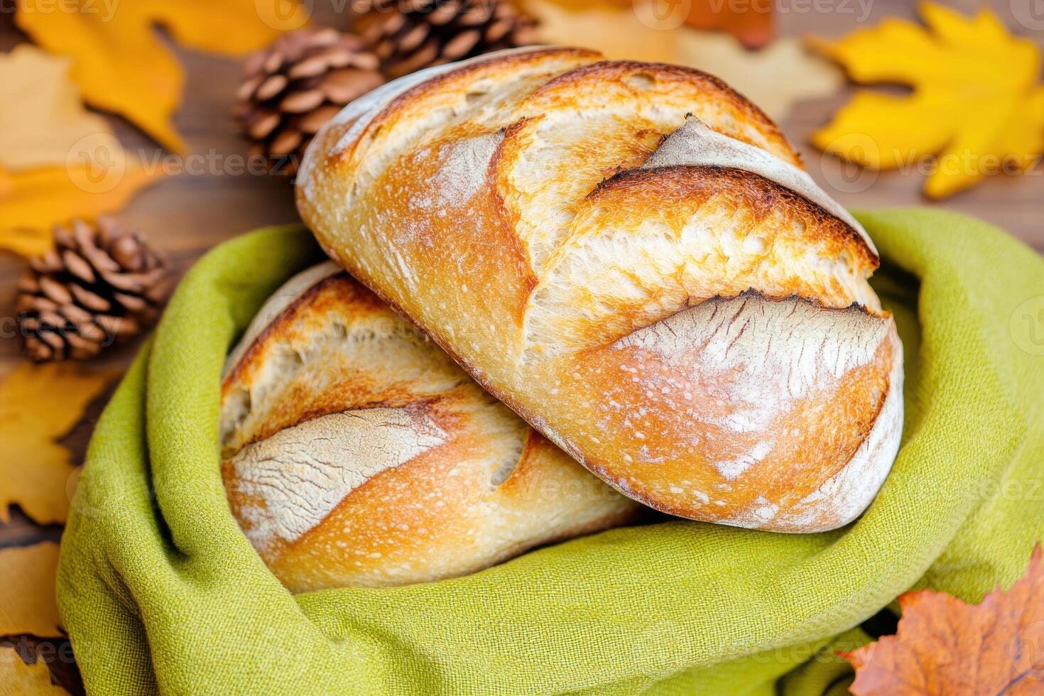 Freshly baked artisan bread stack wrapped in olive-green cloth surrounded by autumn leaves photo