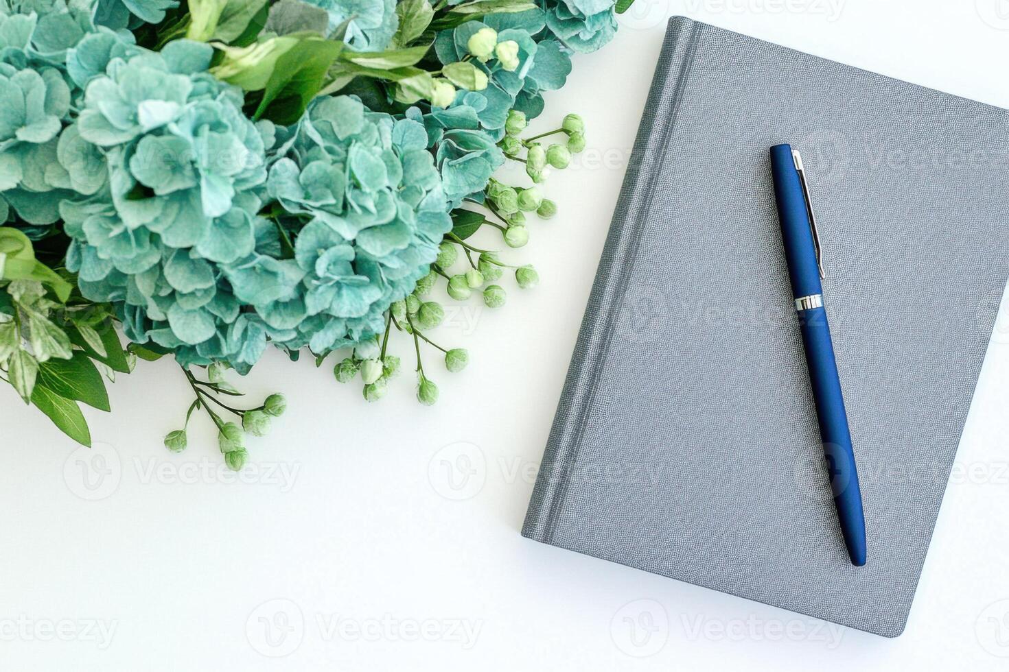 Elegant flat lay featuring turquoise flowers, a gray notebook, and a navy blue pen arranged on a pristine white surface photo