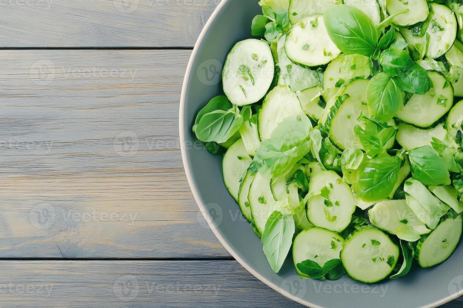 Fresh garden salad with avocado slices and herbs served in a gray ceramic bowl on a wooden table photo