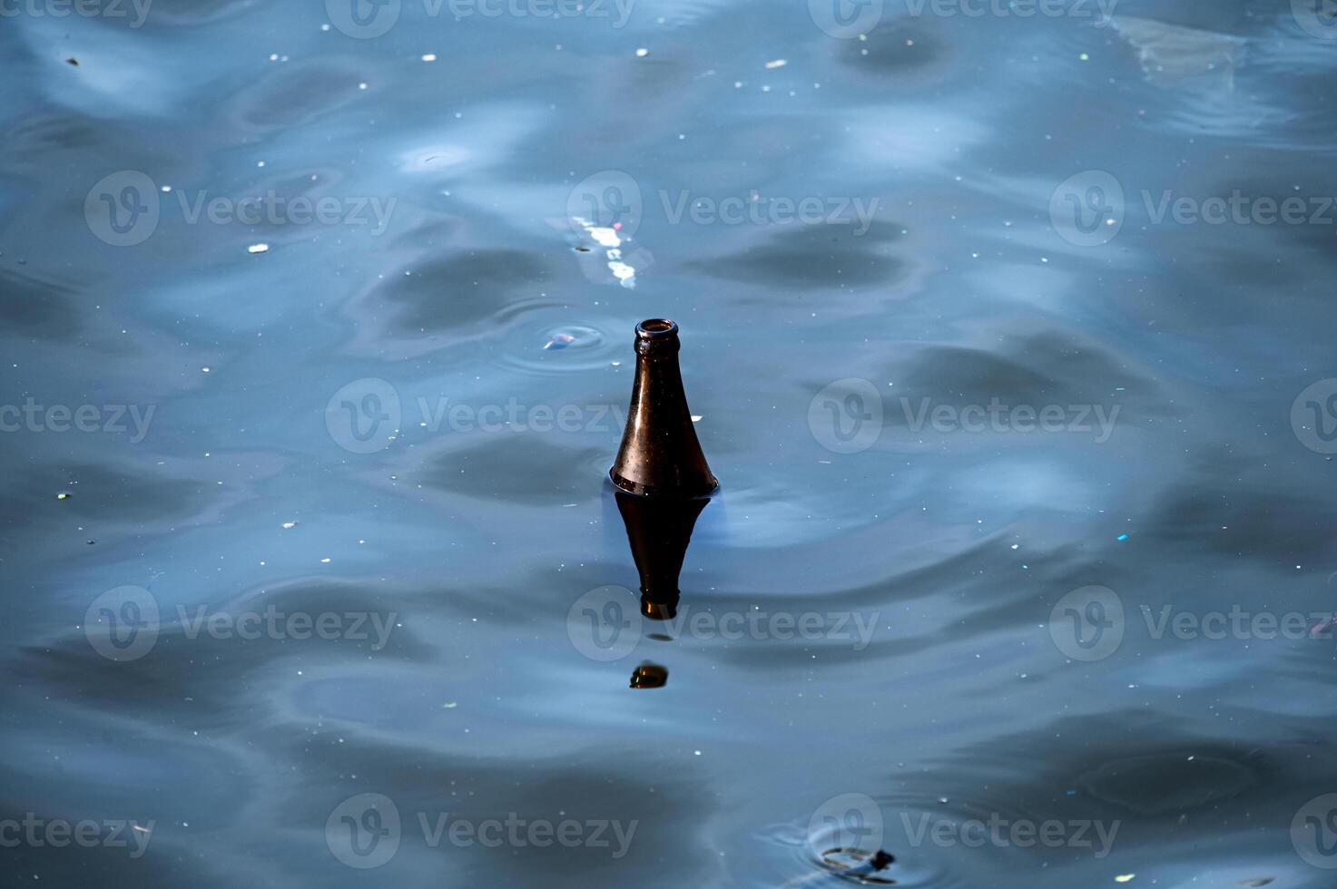 Used glass bottle floating in dirty river photo
