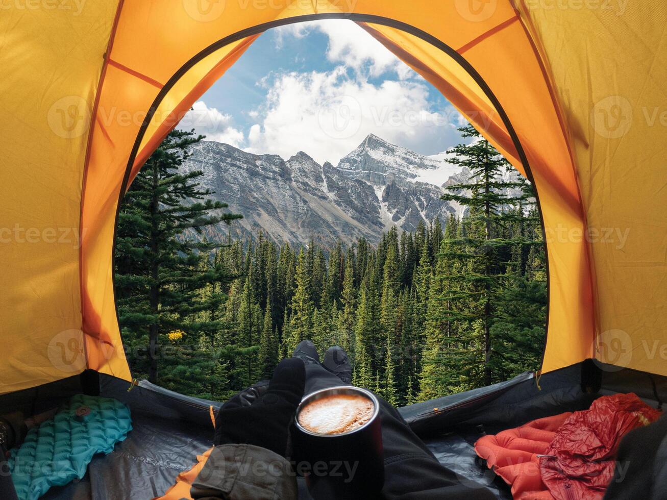 Traveler lying and holding coffee cup in yellow tent and enjoy the view of forest and mountain in national park photo