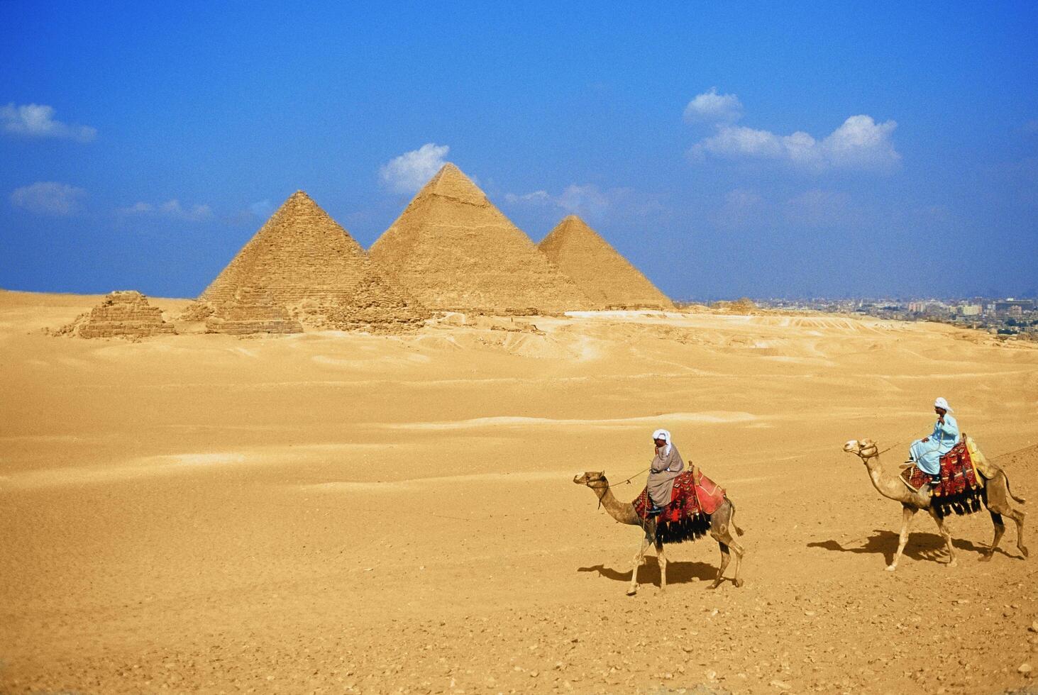 Two people riding camels in front of the pyramids photo
