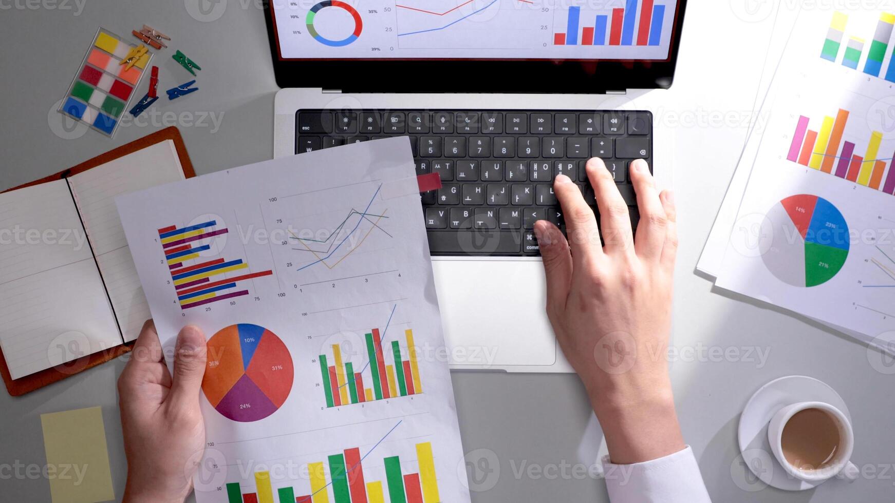 A person is using a laptop with graphs and papers photo