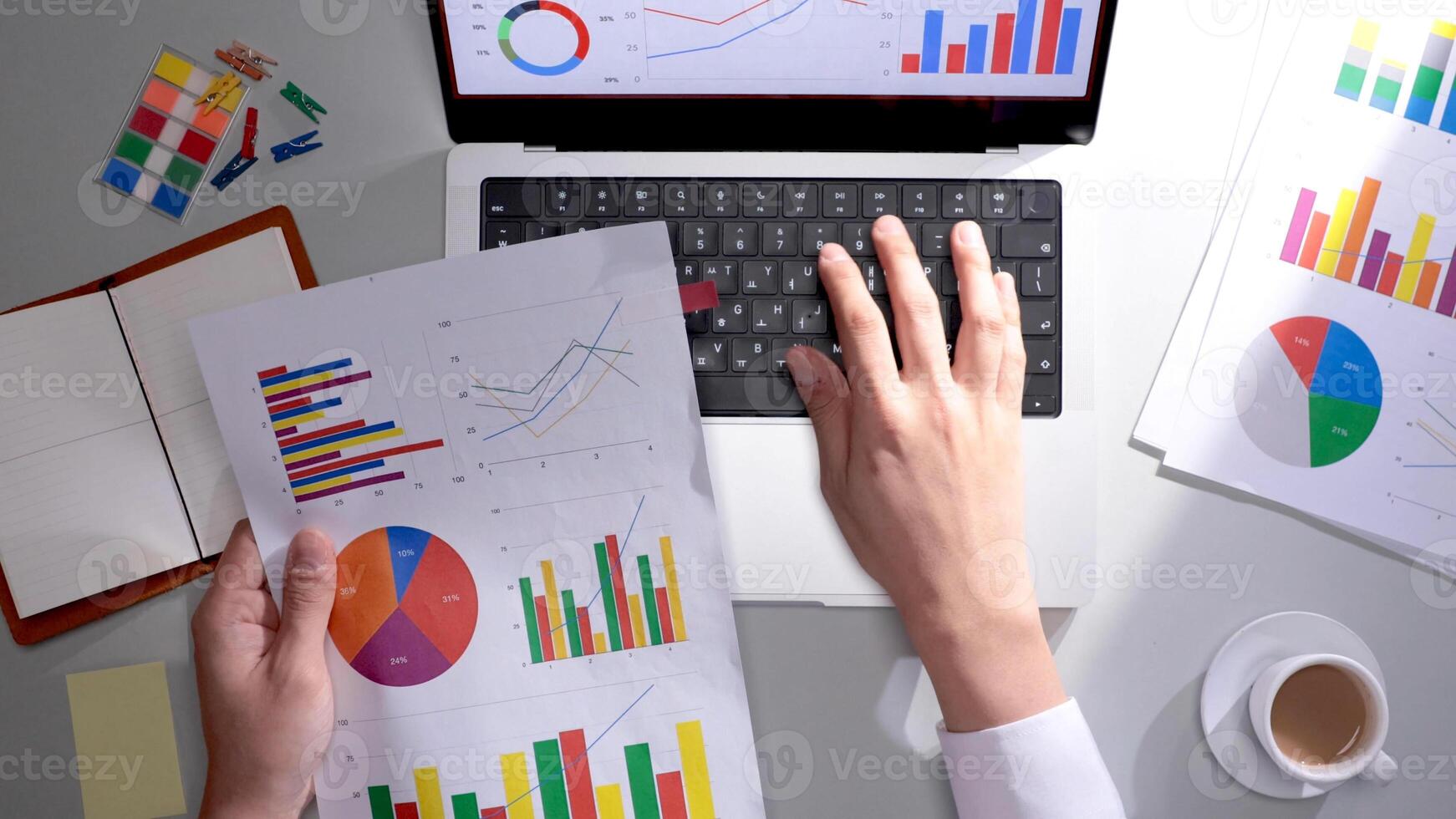A person is using a laptop with graphs and papers photo
