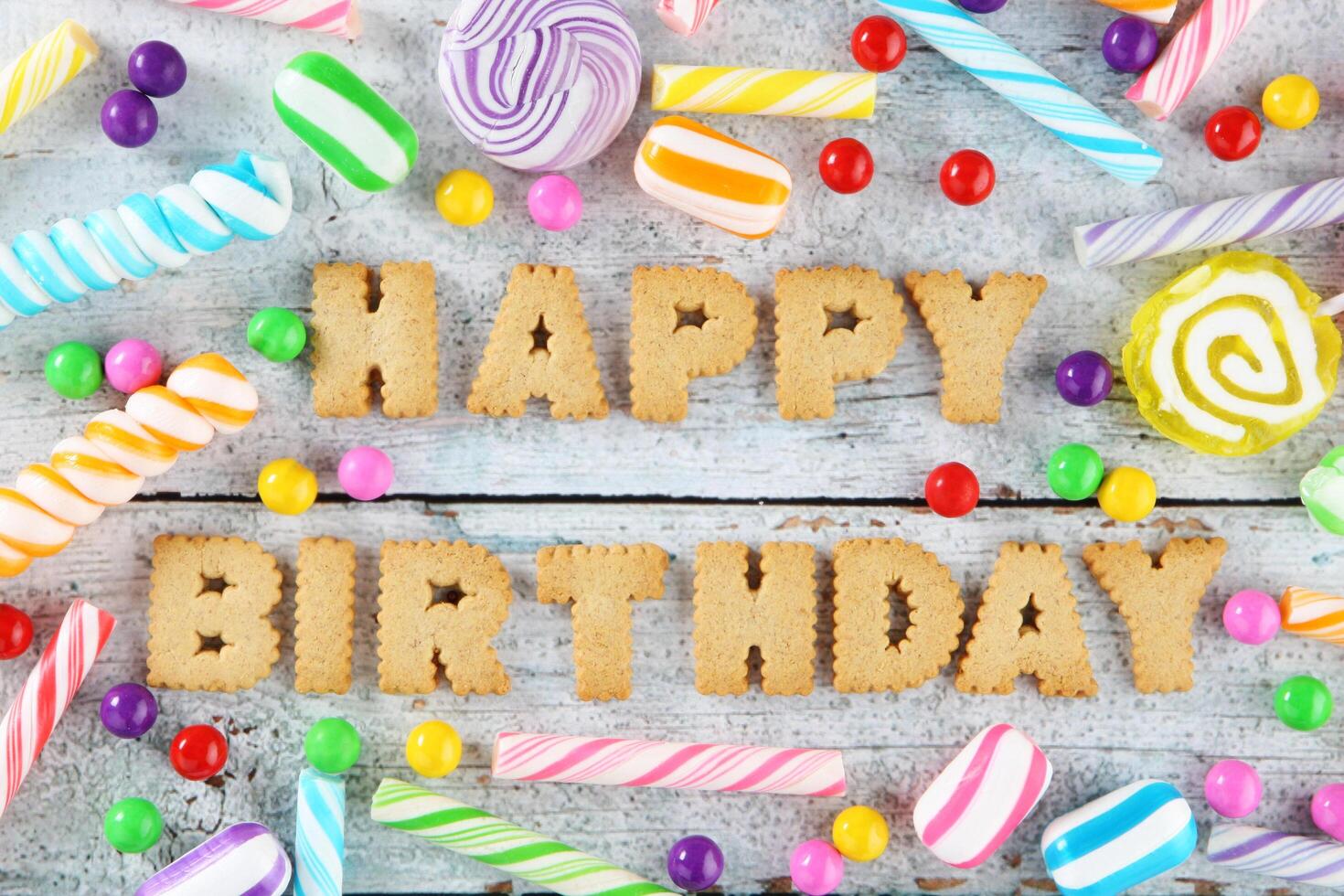 Happy birthday text surrounded by colorful candies and lollipops on a wooden background photo