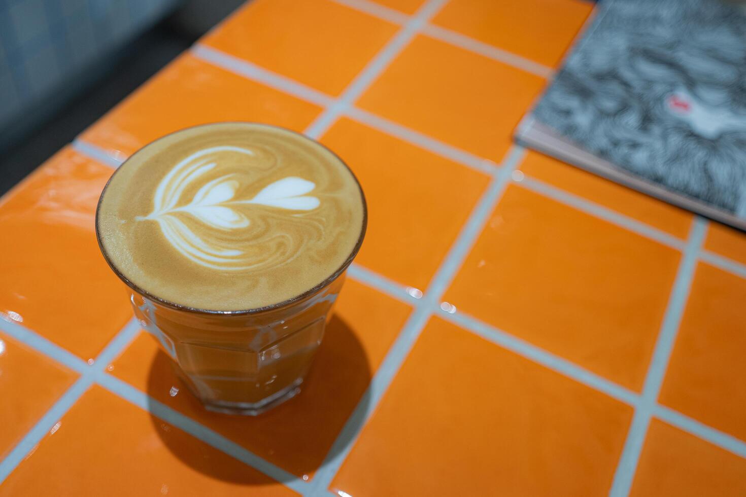 Top view of hot latte coffee with latte art in a glass on orange tile table, copy sapce concept. photo