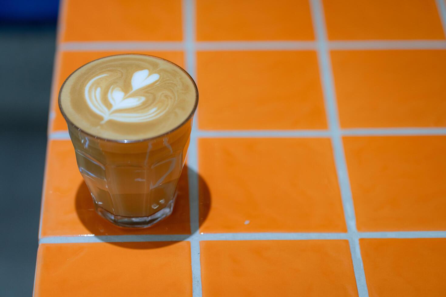 Top view of hot latte coffee with latte art in a glass on orange tile table photo