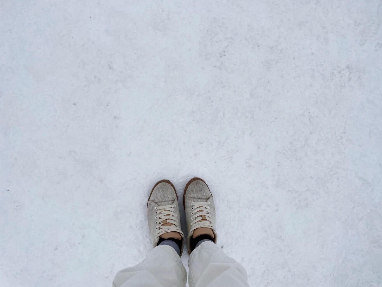 Top of legs in white jeans and brown sneakers on white snow in copy space concept. photo