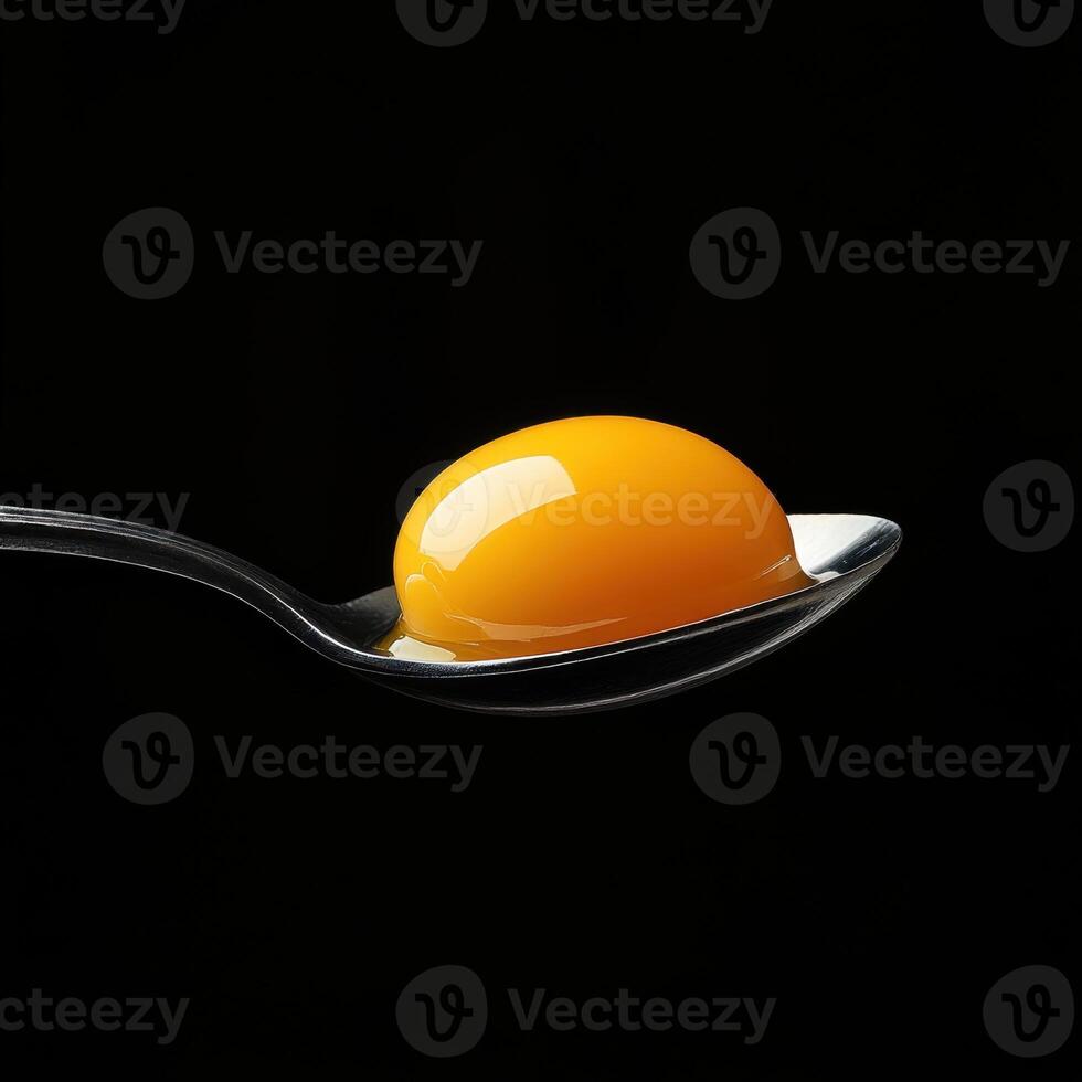 A close-up shot of a raw egg yolk resting in a spoon, isolated on a dark black background photo