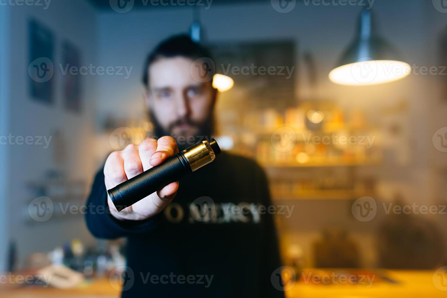 Young beard man show vaping device on his outstretched hand in camera. Selective focus. Vaping concept. Copy space. photo