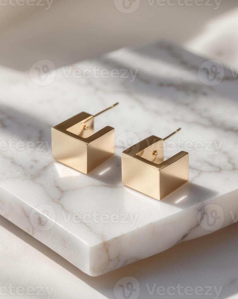Modern abstract gold earrings in geometric cube shapes resting elegantly on a polished marble slab. photo