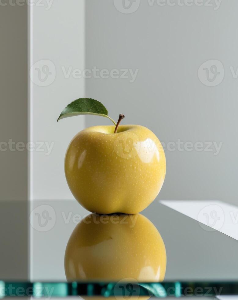 Golden apple with stem and leaf sits on a reflective surface. photo