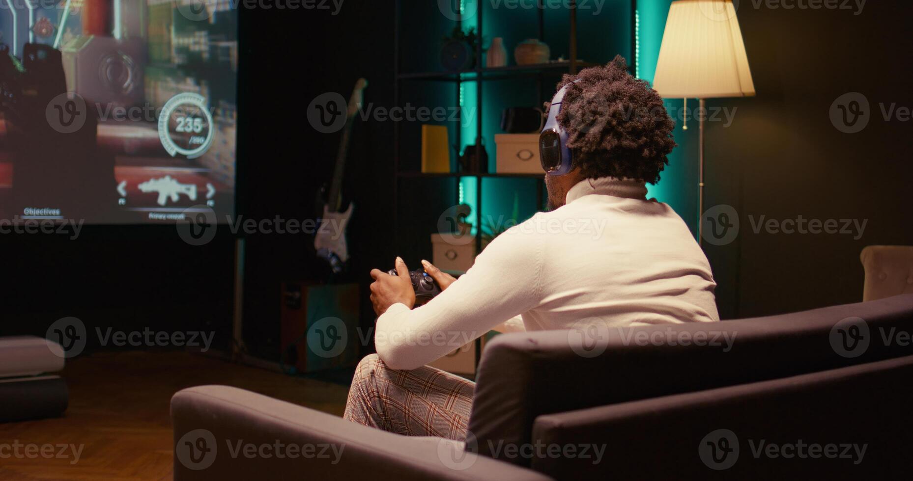 African american man plays videogame on big TV with automatic gun shooting laser bullets at flying robotic foes. Gamer partakes in PvP online multiplayer game tourney on television set, panning shot photo