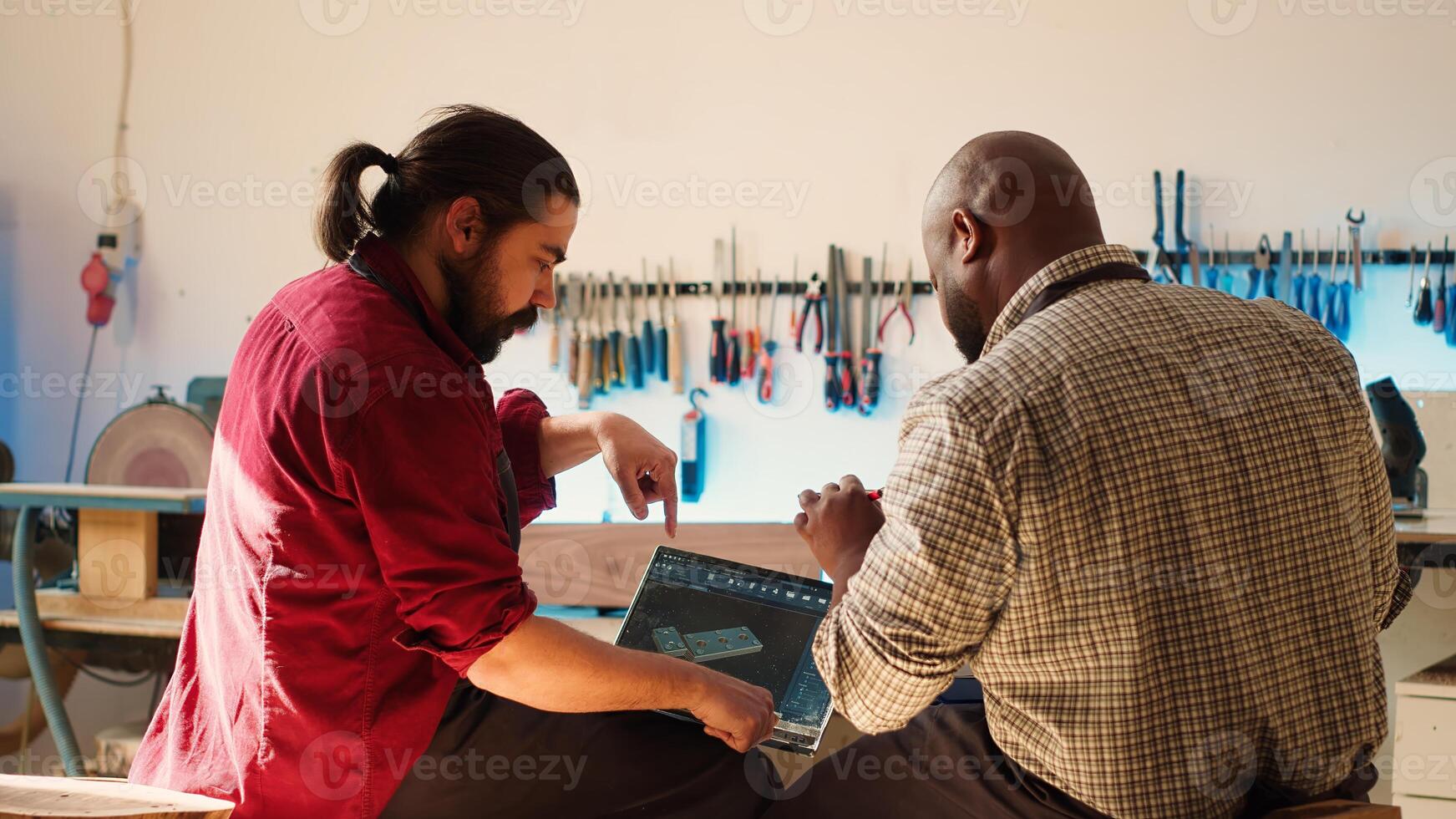 BIPOC artisan and apprentice comparing wood art piece schematic with CAD software 3D render on laptop. Woodworking experts in studio crosscheck drawing on clipboard with notebook blueprint, camera A photo