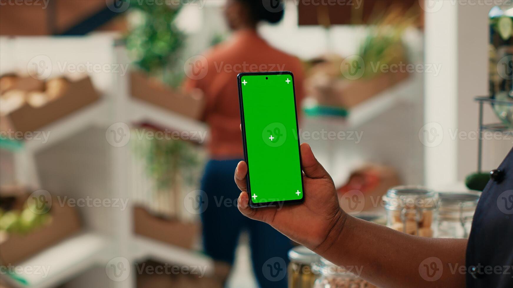 Vendor showing phone with greenscreen layout at supermarket, holding blank copyspace mockup on display. African american seller working at local grocery store, isolated chromakey screen. photo