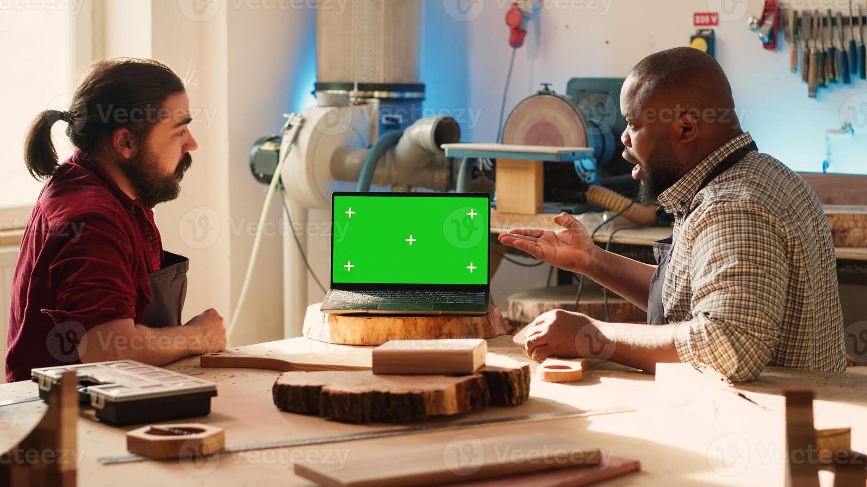 BIPOC artisan and apprentice compare wood art piece with schematic displayed on green screen laptop. Woodworking experts in studio crosschecking wooden object with mockup notebook blueprint, camera A photo