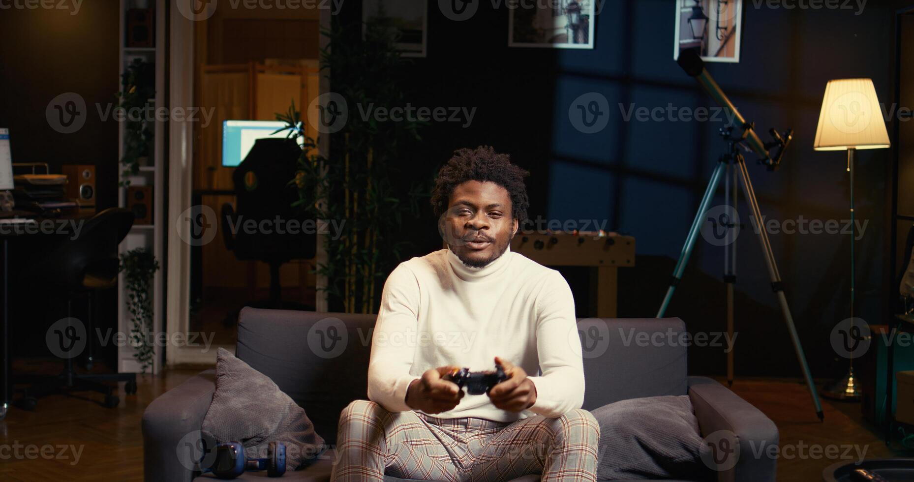 Gamer arriving home, ready to start game and enjoy leisure time. African american man sitting on couch in living room, playing videogame on gaming console, relaxing after work photo